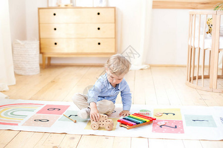 男孩在玩木车儿童益智木制玩具一个男孩坐在斯堪的纳维亚风格儿童房地板上的肖像生态玩具图片