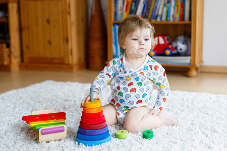 可爱漂亮的小女婴在家里或托儿所玩教育木制玩具蹒跚学步的孩子与五颜六色的堆栈金字塔和音乐玩具快乐健康的孩子图片