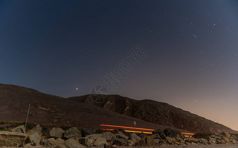 在下面的高速公路上闪烁着头灯猎户座和其他恒星在夜空图片