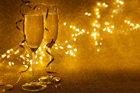 两杯香槟的前视图在金色闪发光的背景上装饰着彩带图片