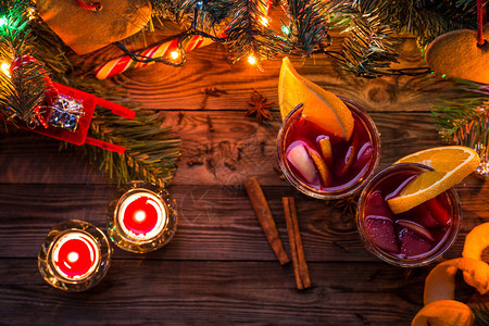 两杯含橙色切片的面包红酒蜡烛和圣诞树背景图片