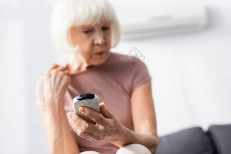 在家感觉热时拿着空调遥控器的老年妇女背景图片