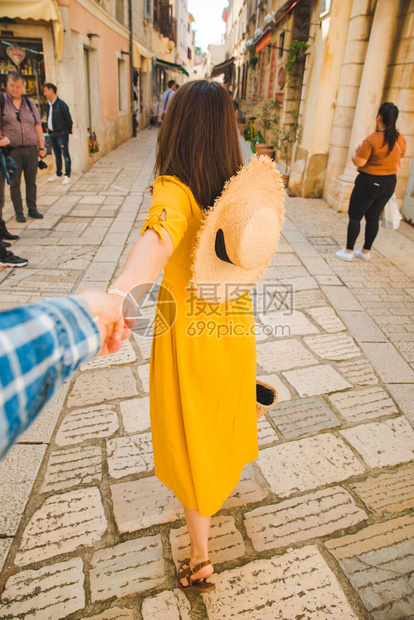 穿着黄色防晒帽的草帽女人在小度假村城市街上走来去牵着男图片