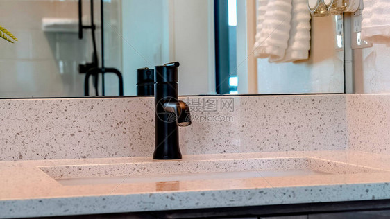 家庭浴室内白色台面上带黑色水龙头的全景框架台下水槽墙上的镜子映出挂着的毛巾敞开的门图片