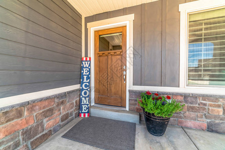 棕色前门与玻璃窗格和欢迎标志反对灰色和石墙在房子的入口处还可以看到灰色的门垫带花背景图片