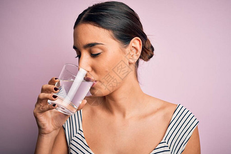 年轻美丽的黑发美女喝杯健康水站在孤立的粉红背景上清新背景图片