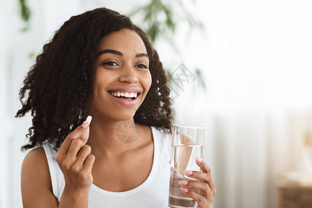 健康饮食营养微笑的非洲女人的肖像拿着维生素丸和一杯矿泉图片