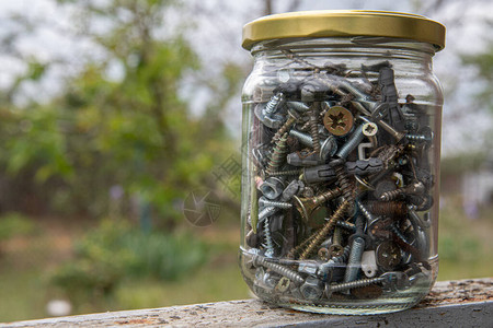 各种紧固件螺栓和螺母的旧罐子通过散景背上模糊的玻璃特写图片
