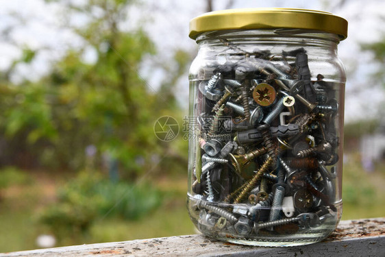 各种硬件螺栓和螺母的玻璃罐通过散景背上的模糊玻璃与复制空间特写金属制品图片