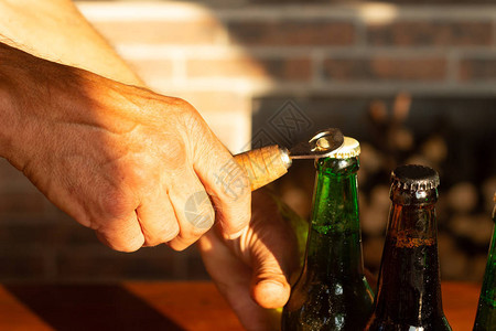 男人的手打开了棕色和绿色冰冷啤酒瓶图片