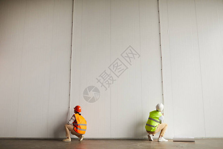 在建筑工地空楼白墙上用铁丝线工作的两名身穿反射服的工人的近图片