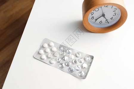 白桌背景上的闹钟和药丸泡罩包装图片