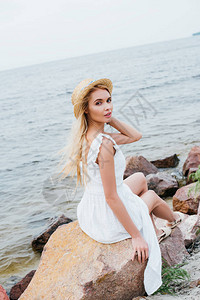 美丽的金发美女在穿着白裙子坐在石头图片
