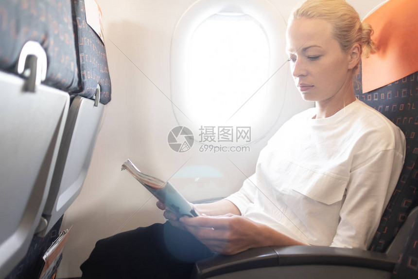 在飞机上阅读飞行杂志的女人坐在客舱里看书的女旅行者阳光透过图片