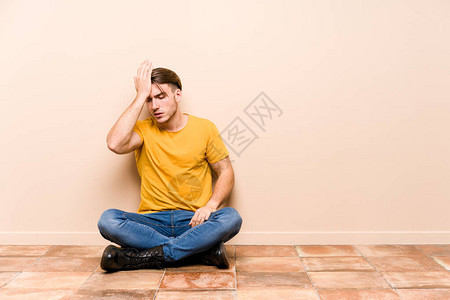 坐在地板上的年轻caucasian男子孤立地忘记了某些东西图片