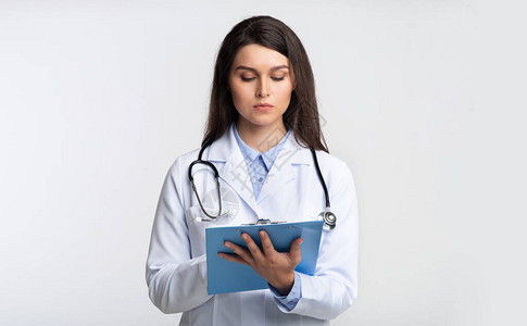女士持有书文件夹阅读医学报告站在灰色工作室背景图片