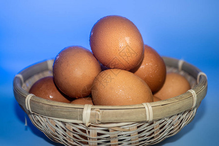 在藤篮中凝结水的新鲜鸡蛋在蓝色背景上背景图片