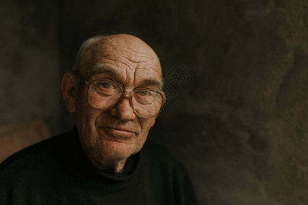 戴着眼镜头发灰白的沉思老人看着别处皱纹智慧在深灰色的纹理墙上光头