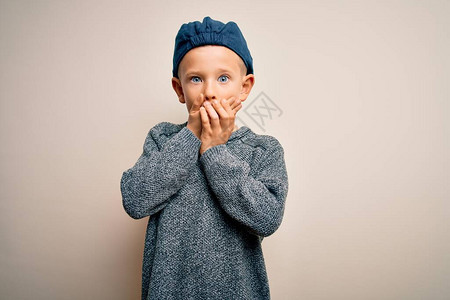 蓝眼睛的黑人小孩穿着羊毛帽在孤立的背景下用双手遮住嘴顶大惊小怪图片