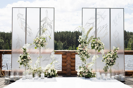 与白色透明屏幕和鲜花和蜡烛的婚礼带羽毛和白玫瑰的两个屏风的图片