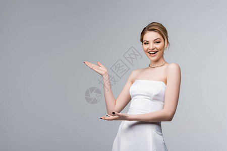 穿着白色婚纱的快乐年轻新娘用双手指着灰色背景图片