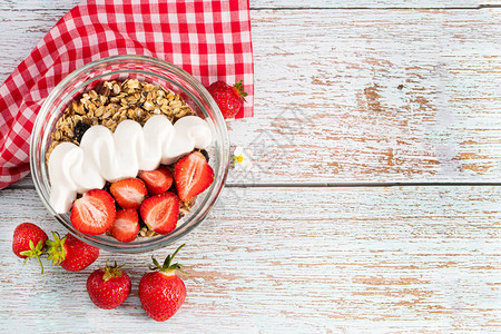 一碗燕麦格兰诺拉麦片配酸奶新鲜草莓和坚果放在白木板上图片