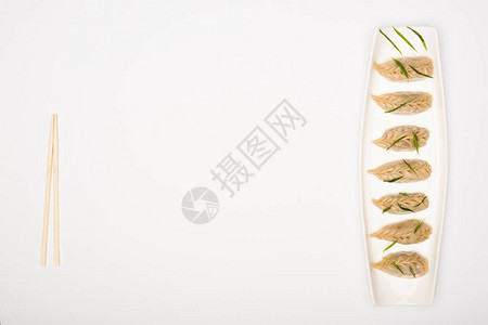 白色背景筷子附近盘子上美味的水饺的顶部视图图片