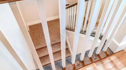 全景作物白色木制栏杆和棕色楼梯的U形楼梯扶手踏板和平台上铺有地毯的楼梯通向带有棕色图片