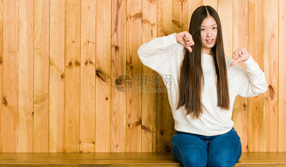 年轻的女人坐在一个木制地方低头伸出拇指图片