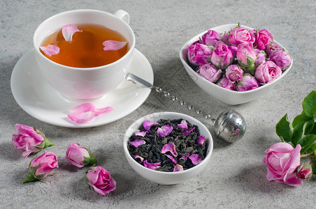 在灰色纹理的桌子上放着花瓣和玫瑰花蕾的茶杯图片