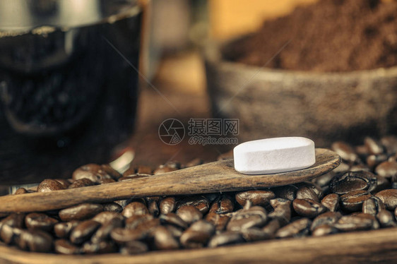 木勺中的咖啡因丸烤咖啡豆一杯黑咖啡和背景木碗图片