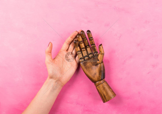 白人女高加索手握着粉红色木制背景上的黑色木制手社区的共图片