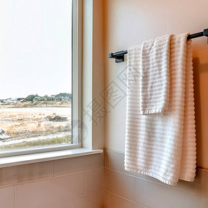 白色毛巾挂在手持瓷砖的卫生间墙上的黑棍上图片