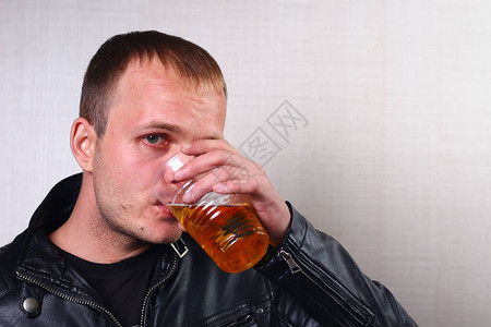 一个穿皮夹克的年轻人喝着一个塑料透明玻图片