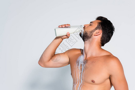 在灰色上喝新鲜牛奶的肌肉大胡子男人图片