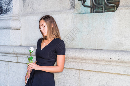 等你身穿黑色短袖V领连衣裙手持白玫瑰花的东欧年轻女子图片