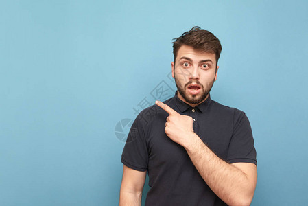 带着胡子和黑衬衫的令人惊讶的成年男子发现一只手指对着空白的脸部图片