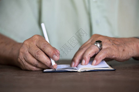 老人在白色笔记本上手写字母木质背景白色铅笔特写和宏观拍摄选择聚图片