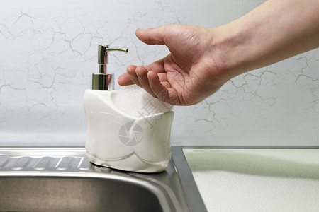 用手从水槽上的撒布器中取出液肥皂图片