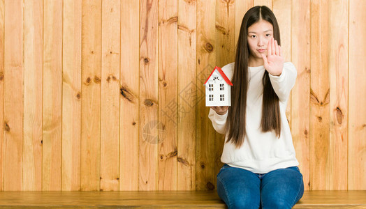 年轻的亚洲女人拿着一栋房子的图标站着伸展的手显示停图片