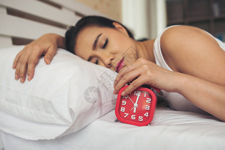 懒女人手拿着闹钟在床上图片素材