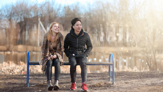 一对年轻人在公园里相遇恋人坐在城市公园的长椅上一个亚裔男孩和一个