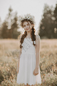 肖像一个穿着白色裙子的年轻女孩和夏季田里的花圈Boho风格添加了小粒子图片