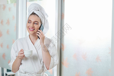 可爱漂亮的年轻美女在洗完澡和电话交谈后喝清晨咖图片
