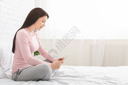 千年妇女浏览数字平板电脑坐在床上侧视空位图片