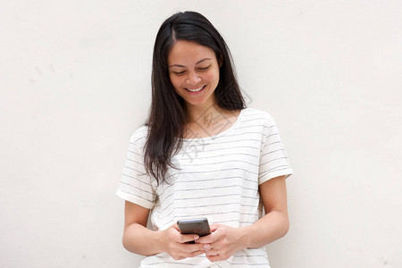 年轻亚洲女在看手机和白背景微笑时的肖像图片