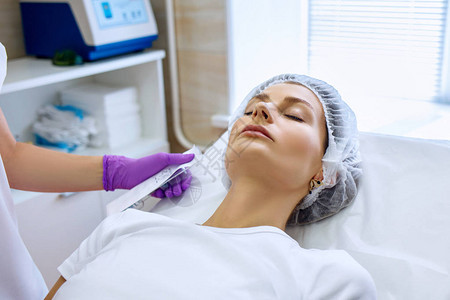 在美容诊所接受复健手术的漂亮女孩注射填充剂穿紫色手套的医生图片