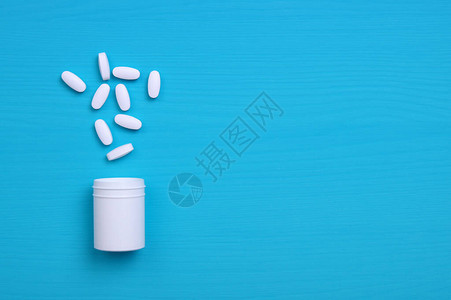 蓝色背景上的各种药丸片剂和胶囊以及白色瓶子图片