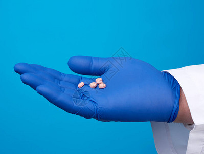 带蓝色消毒手套的男手持有圆环粉红色药丸治疗疾病的概图片