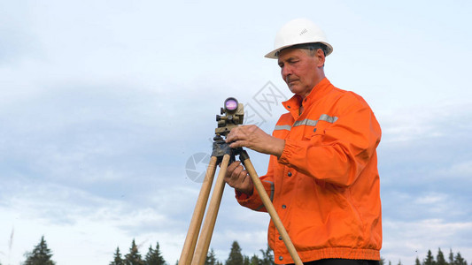 蓝天下大地测量设备附近智能手机上身着橙色连身衣的熟练探险家图片